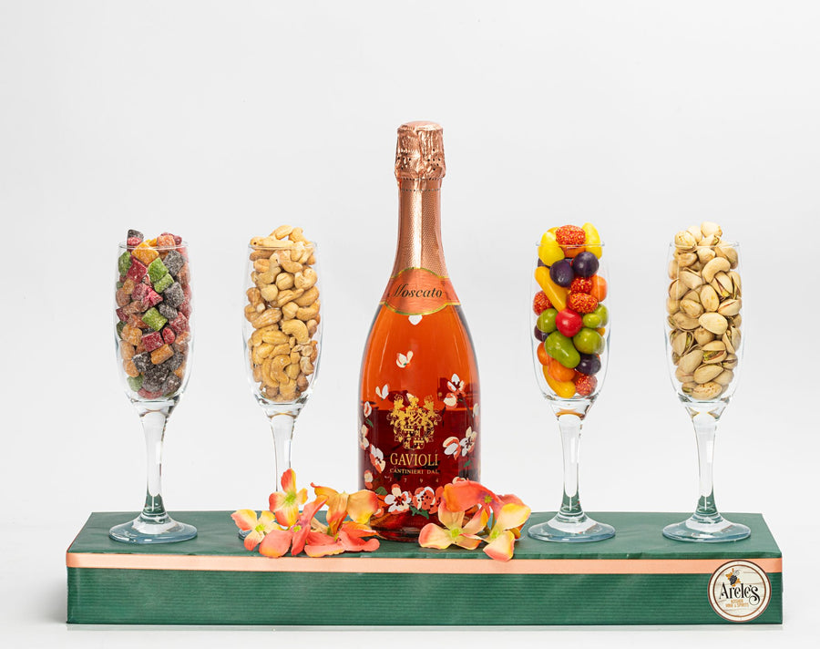 Image contains an arrangement with 4 glasses fulled with nuts candy and dried fruits - the middle boasts a pink moscato champagne.